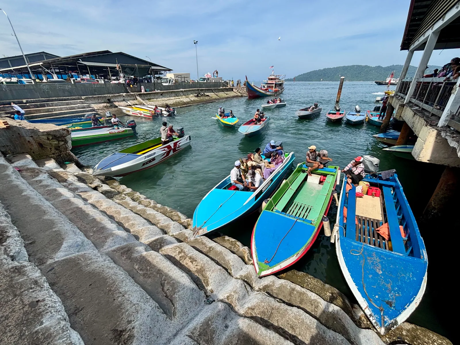 Colorful passenger boats at Kota Kinabalu's fish market jetty, with Gaya Island beyond.